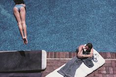 a man laying on top of a towel next to a swimming pool with a woman in the background