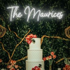 a white wedding cake sitting on top of a table next to candles and flowers in front of a neon sign