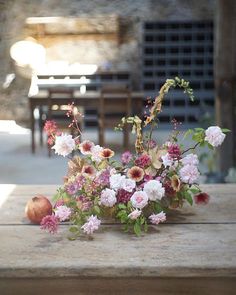 an arrangement of flowers and fruit on a wooden table in front of a stone building