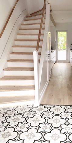 a white kitchen with black and white flooring next to a stair case that leads up to the second floor