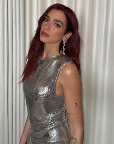 a woman with red hair and piercings posing for a photo wearing a silver dress