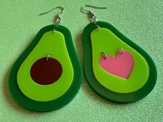 two green and pink earrings with an avocado cut in the middle on a table