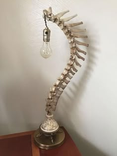 a skeleton lamp on top of a wooden table next to a white wall with a light bulb hanging from it's side