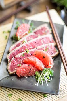 sliced up meat and vegetables on a black plate with chopsticks next to it