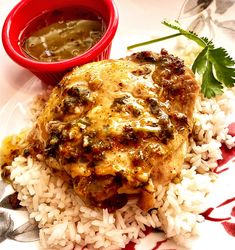 a white plate topped with rice and meat covered in gravy next to a red bowl