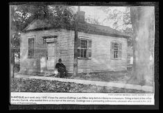 an old black and white photo of a man sitting in front of a small house