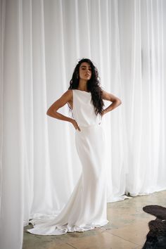 a woman standing in front of a curtain wearing a white dress and long black hair