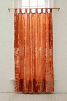 an orange curtain hanging in front of a window with a white wall and wooden frame