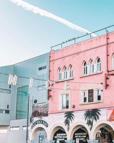 an old pink building with palm trees on the front and side, next to other buildings