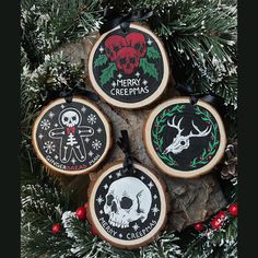 three christmas ornaments hanging from a tree with pine branches and berries around them, decorated with black and white designs