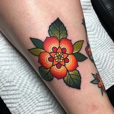 an orange flower with green leaves on the side of her leg, and another tattoo design