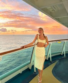 a woman standing on the deck of a cruise ship at sunset with her arms around her waist