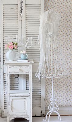 a white table with a dress on it next to a lamp and wallpapered background