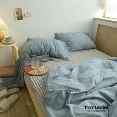 an unmade bed with blue sheets and pillows in a white room next to a window