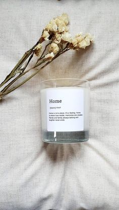 a white candle sitting on top of a bed next to dried flowers