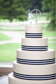 a three tiered white cake with blue stripes and a monogram on the top