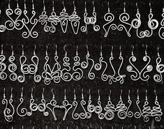 several pairs of earrings hanging from hooks on a black background with white swirls and hearts