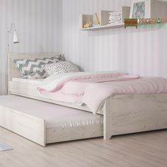 a white bed with pink sheets and pillows on top of it next to a wooden floor