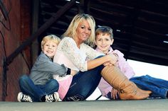 a woman and two boys sitting on the ground with their legs crossed in front of them