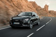 an audi suv driving down the road with mountains in the backgrounds