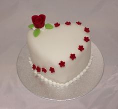 a white heart shaped cake with red flowers on it's edges and frosting