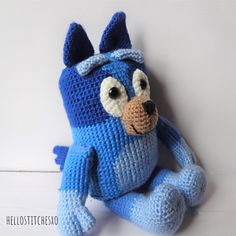 a crocheted blue stuffed animal sitting on the floor with its eyes wide open