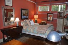 a bedroom with red walls and pictures on the wall, including a bed in front of a mirror