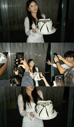 the woman is taking pictures with her cell phone while she holds up a white cake