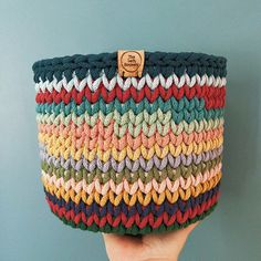 a hand holding up a multicolored crocheted basket on a blue background