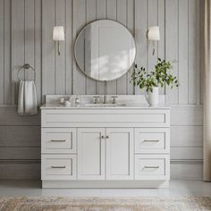 a white bathroom vanity with a round mirror above it and plants in vases on the counter