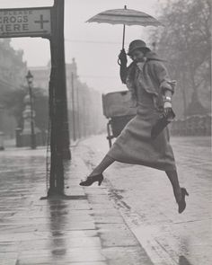 a woman jumping in the air while holding an umbrella over her head on a rainy day