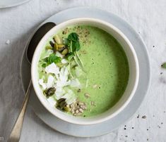 a bowl of green soup on a white tablecloth with spoons and napkins