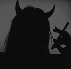 a person with long hair and horns holding a knife in front of their face as they are silhouetted against a dark background