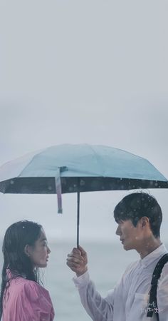 a man and woman standing under an umbrella on the beach in the rain while it is raining