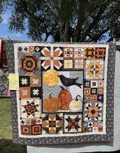 a quilt hanging from a clothes line with pumpkins and birds on it in front of a tree