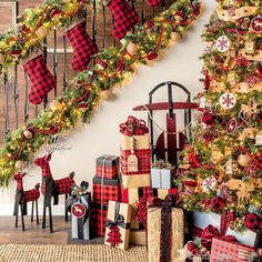 a christmas tree with presents under it next to a banister decorated with red and gold plaid