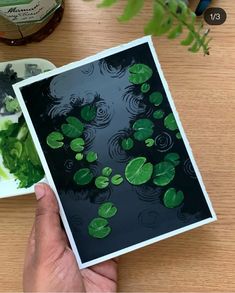 a person holding up a card with water lilies on it and green leaves floating in the water