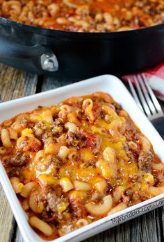 a casserole dish with meat and cheese in it on a wooden table next to a skillet