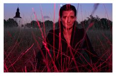 a man sitting in tall grass with a red light on his face and the sky behind him