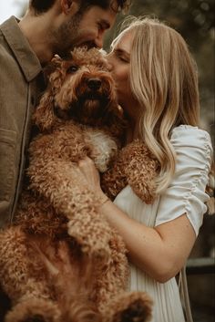 a man and woman kissing while holding a brown poodle dog in front of them