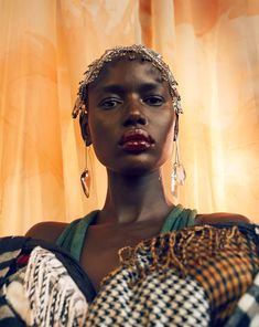 a woman with large earrings and scarves on her head standing in front of a curtain