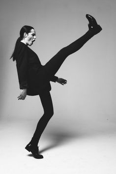 a woman in black is dancing with her legs spread out and one leg bent forward