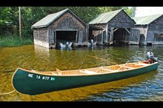 a green canoe sitting on top of a body of water next to wooden shacks