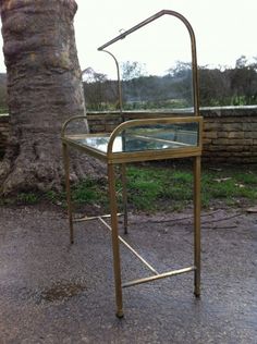 a table with a glass top and metal frame sitting next to a tree in the middle of a park