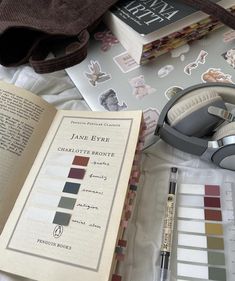 an open book sitting on top of a bed next to headphones and other items