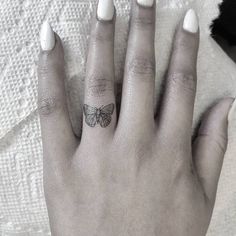 a woman's hand with a butterfly tattoo on it and the other hand has white nails