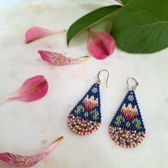 a pair of beaded earrings sitting on top of a table next to pink flowers