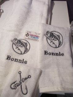 three embroidered towels with fish and name on them are sitting next to each other in the bathroom