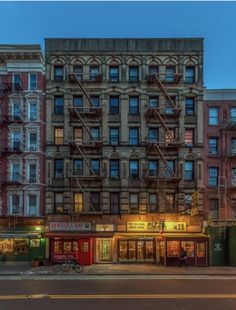 an old building with fire escapes in front of it at night, on the corner of a city street