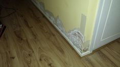 the corner of a room with wood flooring and paint peeling off it's walls